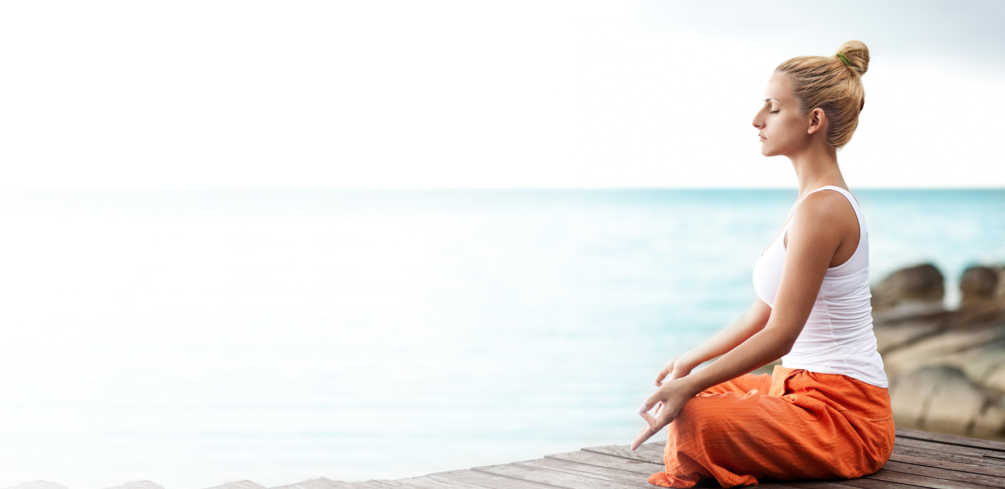 Serene woman sitting near the ocean, representing calm, balance, and healthy skin inspired by the AYU Sunless philosophy.